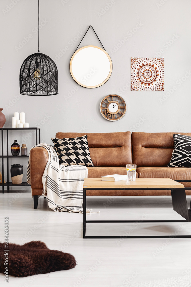 Brown leather couch with blanket and patterned cushions in real photo of  bright living room interior
