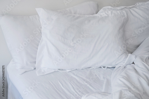 Unmade bed close-up with white bedsheet and pillows.