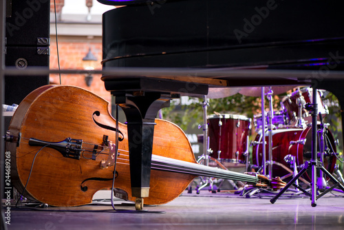 Wooden cello or violin on stage prepared for playing. Classical instruments, piano, drums in background. Concept of orchestra music. Audience waiting for concert to begin