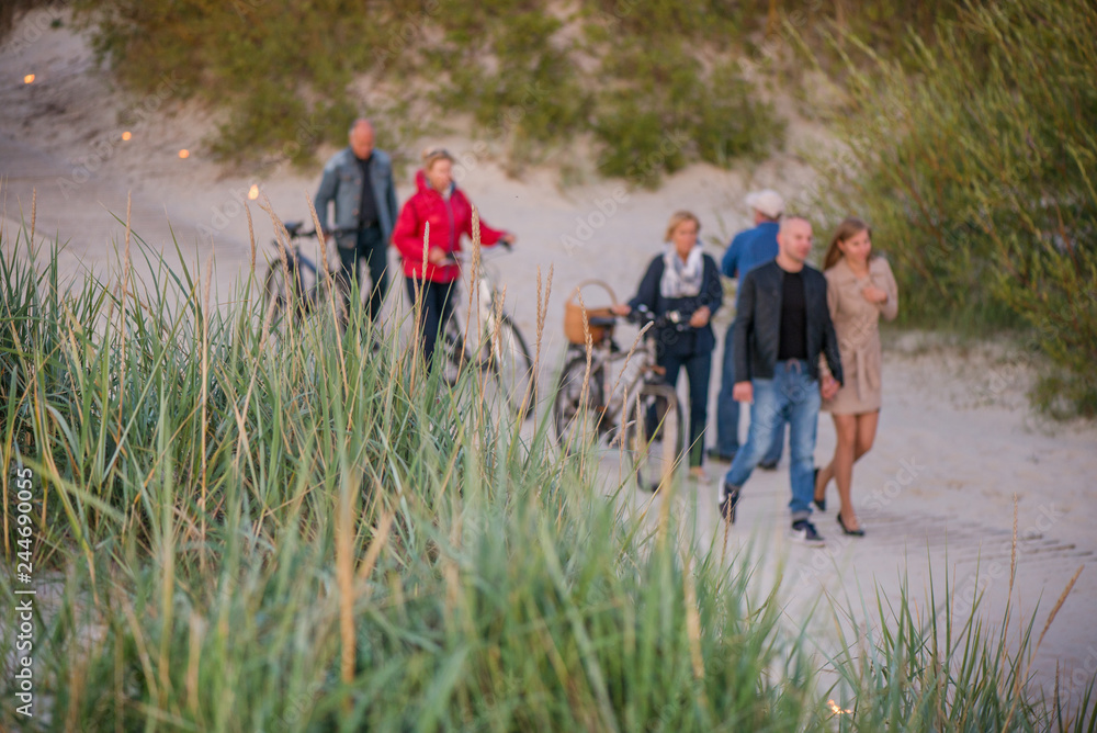 Fototapeta premium Romantic bonfire night at seaside during sunset. People gathering together to celebrate Night of ancient lights. Walking on wooden pathway on seaside on lit candle path during sunset