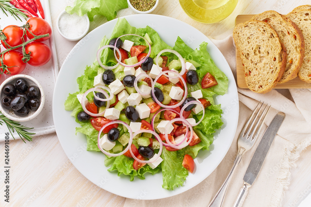 Greek salad on white plate on old rustic white wooden table, fresh salad with tomatoes, cucumbers, feta, onion. Top view Greek salad on white plate on old rustic white wooden table, fresh salad with tomatoes, cucumbers, feta, onion. Top view