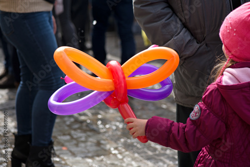 A small girl holding a balloon butterfly or dog that she got as a gift for her birthday party at a children party from clown  