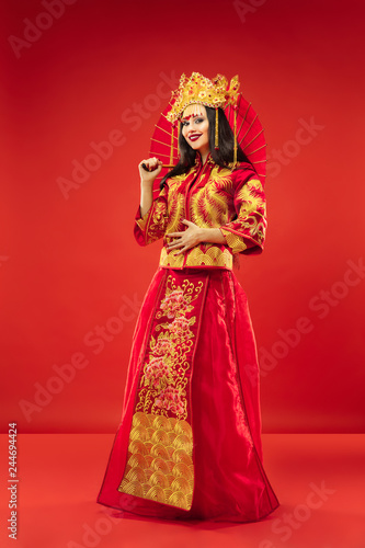 Chinese traditional graceful woman at studio over red background. Beautiful girl wearing national costume. Chinese New Year, elegance, grace, performer, performance, dance, actress, dress concept