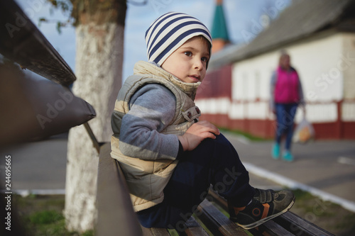little boy sitting on a bench. baby in a striped hat in the city