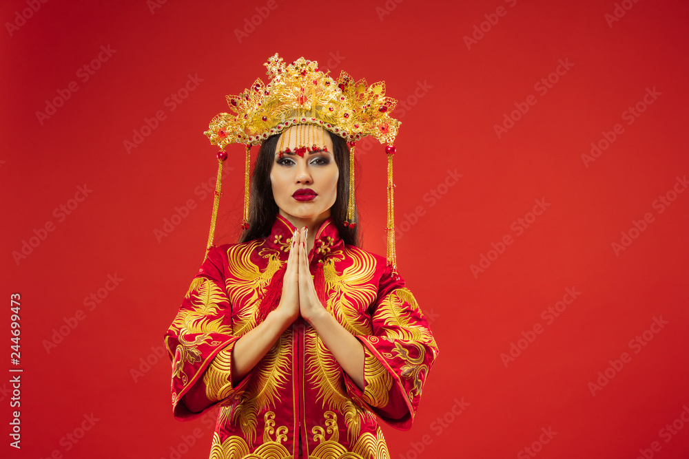 Chinese traditional graceful woman at studio over red background. Beautiful girl wearing national costume. Chinese New Year, elegance, grace, performer, performance, dance, actress, dress concept Chinese traditional graceful woman at studio over red background. Beautiful girl wearing national costume. Chinese New Year, elegance, grace, performer, performance, dance, actress, dress concept