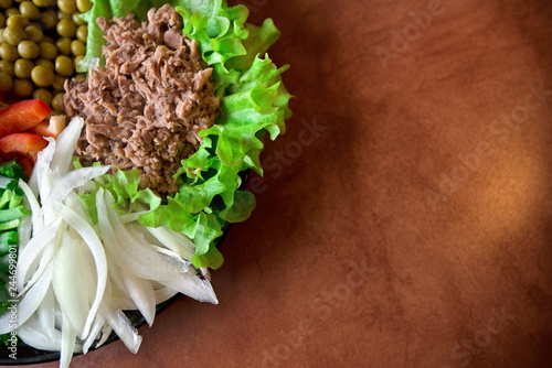 Abstract, blurry shot. Freshly made vegetable salads on plate on rustic background. Tuna with green lettuce, peas, paprika or red pepper, onion slices and spring onions. Delicious meal for breakfast. 