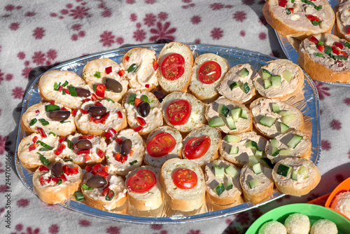 Variety of mini sandwiches with cheese cream, vegetables  roasted cherry tomatoes, olives, cucumber, spring onions, paprika, basil and other herbs. Fresh appetizer canape at the picnic outdoors.  