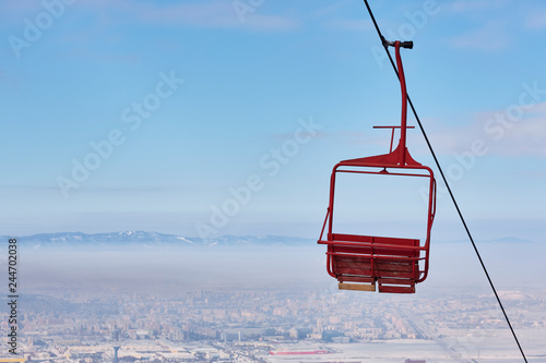 Empty old wooden chairlift against out of focus aerial urban area and blue sky. Brasov, Romania.