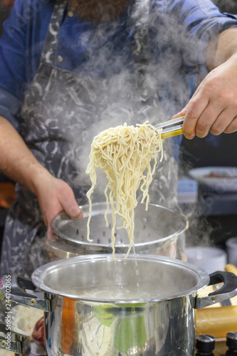 Chef takes out with slotted spoon hot steaming egg noodles from the pan