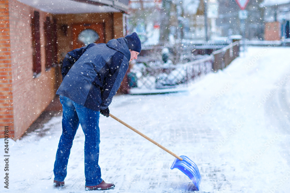 Man with snow shovel cleans sidewalks in winter during snowfall. Winter time in Europe. Young man in warm winter clothes. Snow and weather chaos in Germany. Snowstorm and heavy snowing. Schneechaos Man with snow shovel cleans sidewalks in winter during snowfall. Winter time in Europe. Young man in warm winter clothes. Snow and weather chaos in Germany. Snowstorm and heavy snowing. Schneechaos