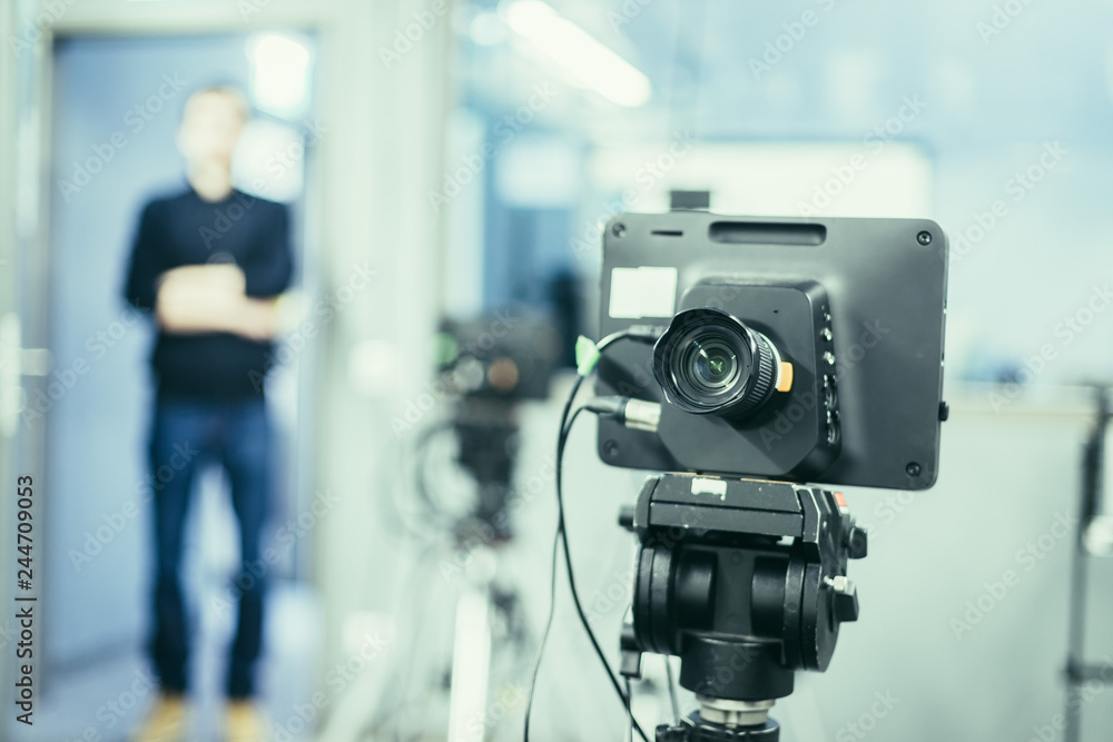 Film camera in broadcasting studio, spotlights and equpiment, director in the background