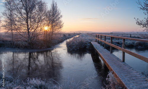 Fototapeta Naklejka Na Ścianę i Meble -  Small footbridge in the frozen Dutch countryside during winters dawn.