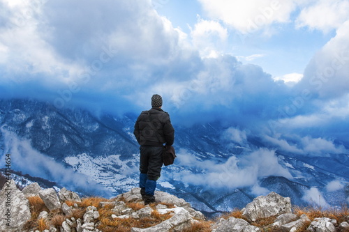 Hiker standing on a mountain top and looking into dynamic sky. Foggy mountain, Colorful winter landscape