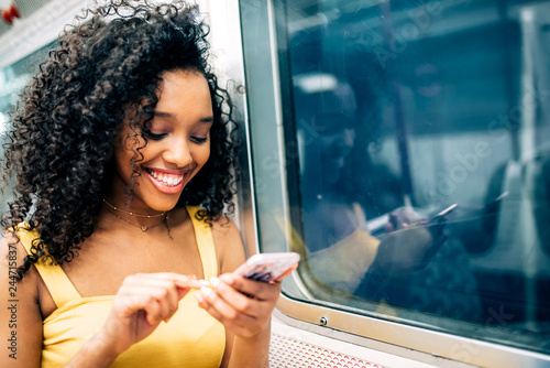 Photography Young black woman sitting inside the underground on the mobile phone