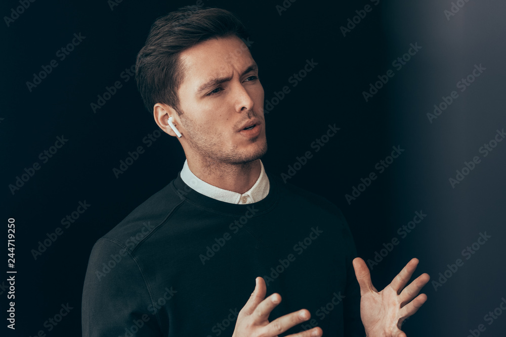Serious young handsome man have a conversation with colleagues during meeting on black background, with wireless earphones. Caucasian businessman using wireless headphones in business conference.