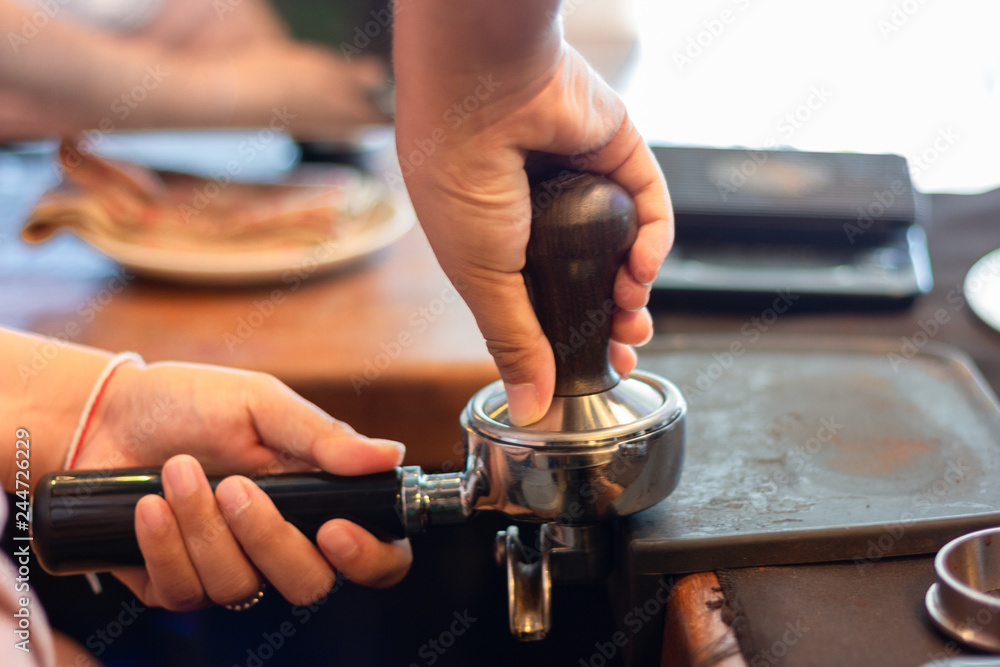 Asian woman barista presses ground coffee using tamper into portafilter , close up hands. Asian woman barista presses ground coffee using tamper into portafilter , close up hands.