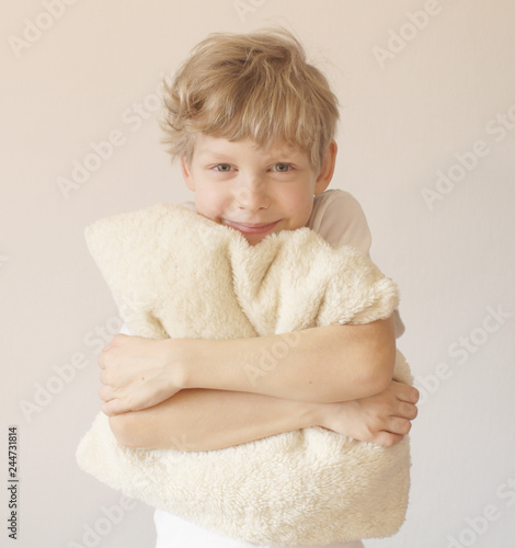 Boy is hugging a pillow. Pillow advertising. Looks into the camera. Nice smile.
