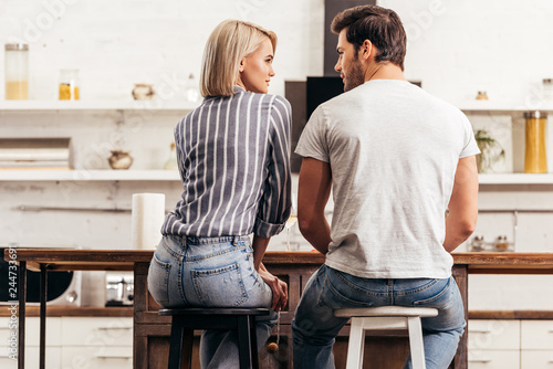 rear view of boyfriend and attractive girlfriend sitting on chairs in kitchen