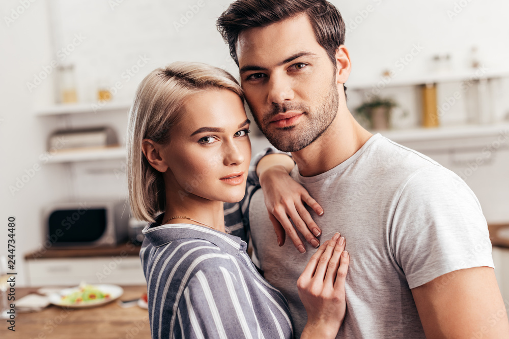 selective focus of handsome boyfriend and attractive girlfriend hugging and looking at camera selective focus of handsome boyfriend and attractive girlfriend hugging and looking at camera