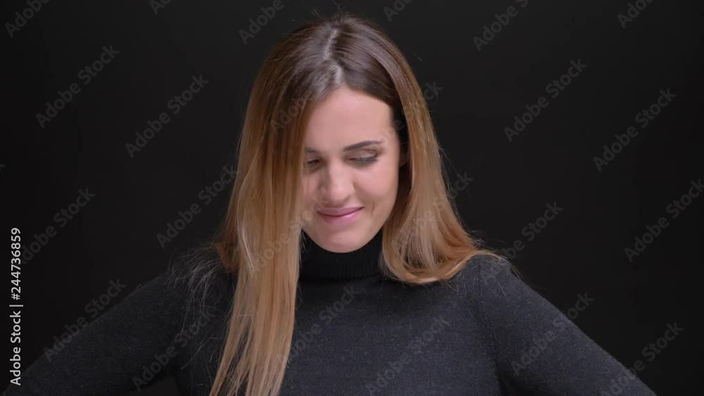 Portrait of young caucasian long-haired blonde girl humbly laughing watching downwards on black background. Portrait of young caucasian long-haired blonde girl humbly laughing watching downwards on black background.