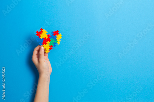 Child hand holding colorful heart on blue background. World autism awareness day concept