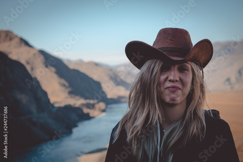 Girl travel in mountains alone. Spring weather, calm scene. Backpacker walking outdoors, view over landscape in sunlight. Wanderlust photo series. Wearing a cowboy hat.