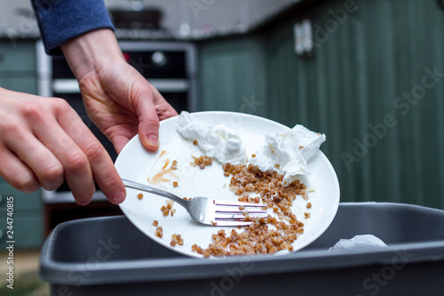 Close up of a person throwing from a plate the leftover of buckwheat to the trash bin. Scraping food waste photo