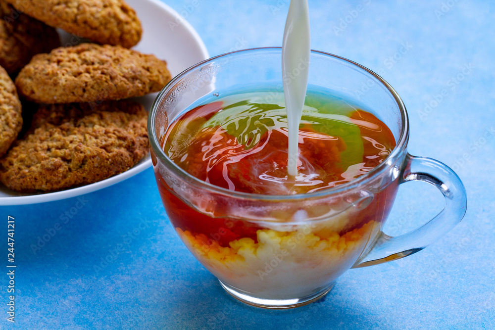 Breakfast with oatmeal cookies and pouring milk into a cup of black tea. Flour, cereal dessert and hot drink Breakfast with oatmeal cookies and pouring milk into a cup of black tea. Flour, cereal dessert and hot drink