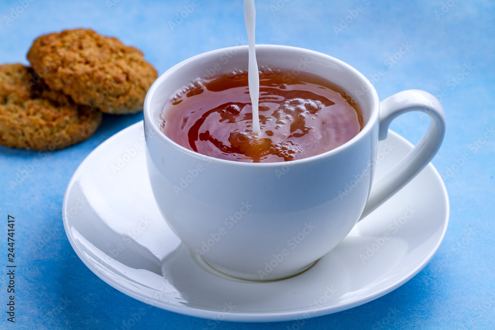 Breakfast with oatmeal cookies and pouring milk into a cup of black tea. Flour, cereal dessert and hot drink Breakfast with oatmeal cookies and pouring milk into a cup of black tea. Flour, cereal dessert and hot drink
