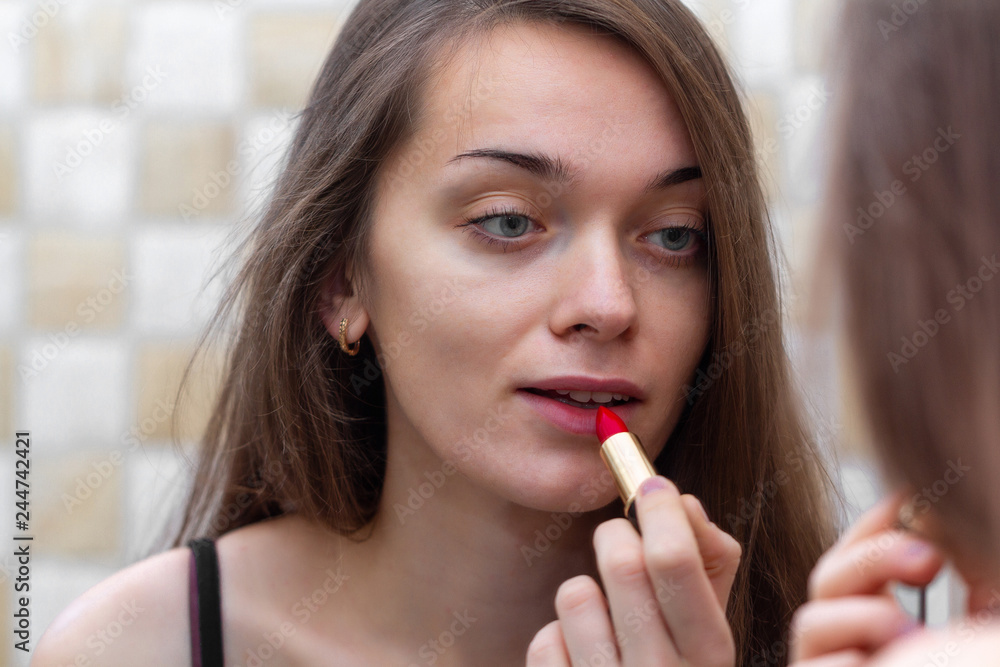 Young, attractive brown haired woman applying red lipstick for lip makeup in mirror. Home and everyday Makeup Young, attractive brown haired woman applying red lipstick for lip makeup in mirror. Home and everyday Makeup