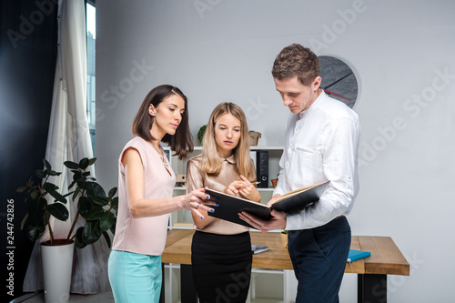 Theme business, teamwork and partnerships. A group of young people, three people, stand in an office near the table in official clothes, work with documents, make praks sign contracts