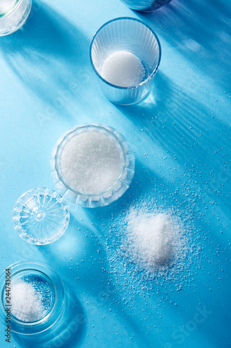 Closeup of scattered sugar and sugar in a glass bottle, on blue background