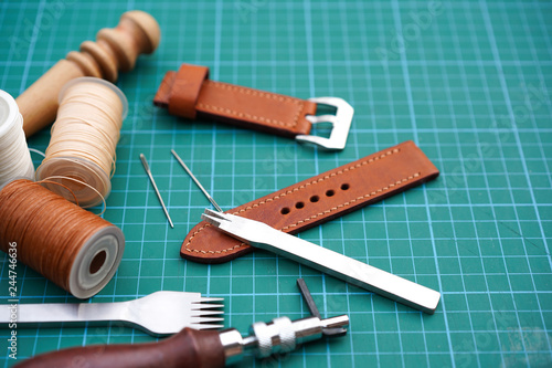 Handmade leather watch strap with pricking iron,stitching thread,burnish and slicker wooden in the leather workshop.Leather craft and DIY crafting tools on craftsman's work desk.Handmade ,DIY Concept. photo