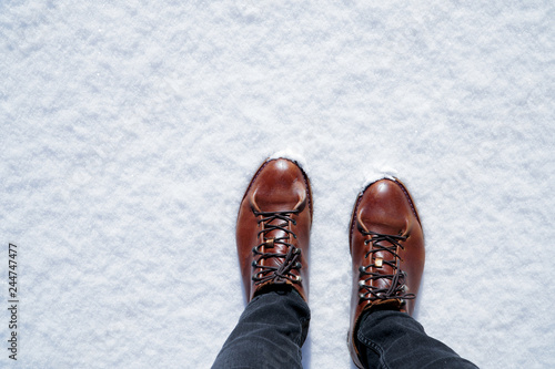 Men's leather boots and black jeans on snow. Brown men's hiking shoes closeup on sunny winter day.Top view with copy space.