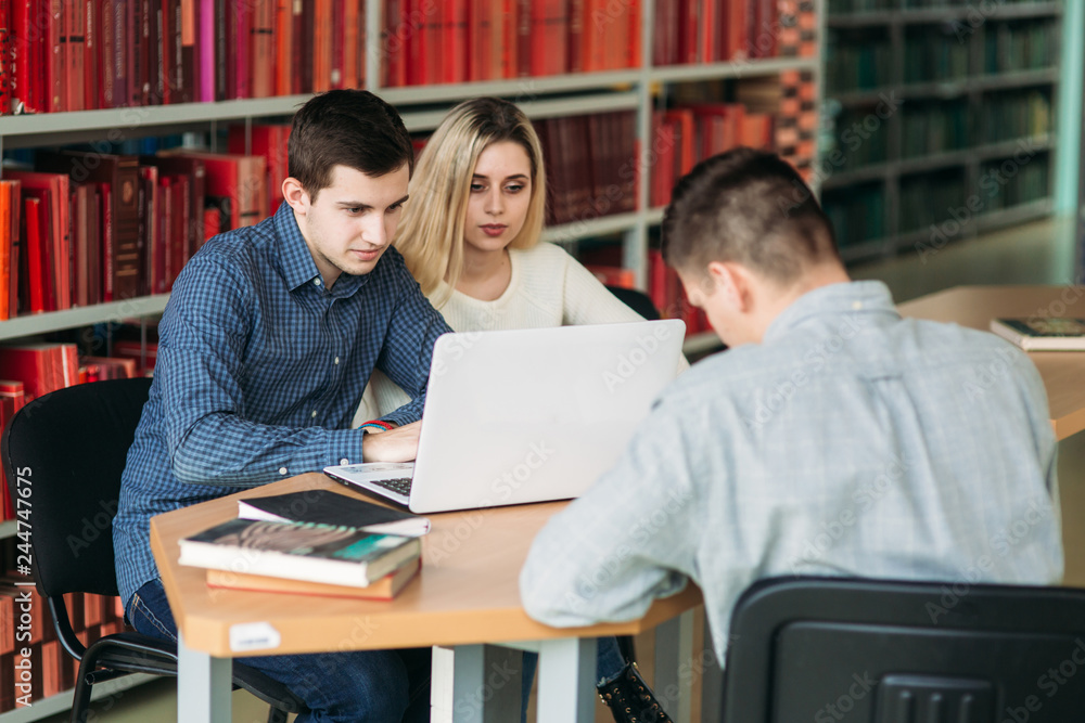 University students sitting together at table with books and laptop. Happy young people doing group study in library University students sitting together at table with books and laptop. Happy young people doing group study in library