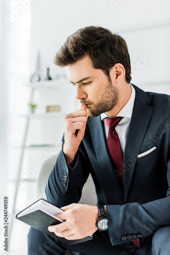 pensive businessman in formal wear sitting and holding notebook in office