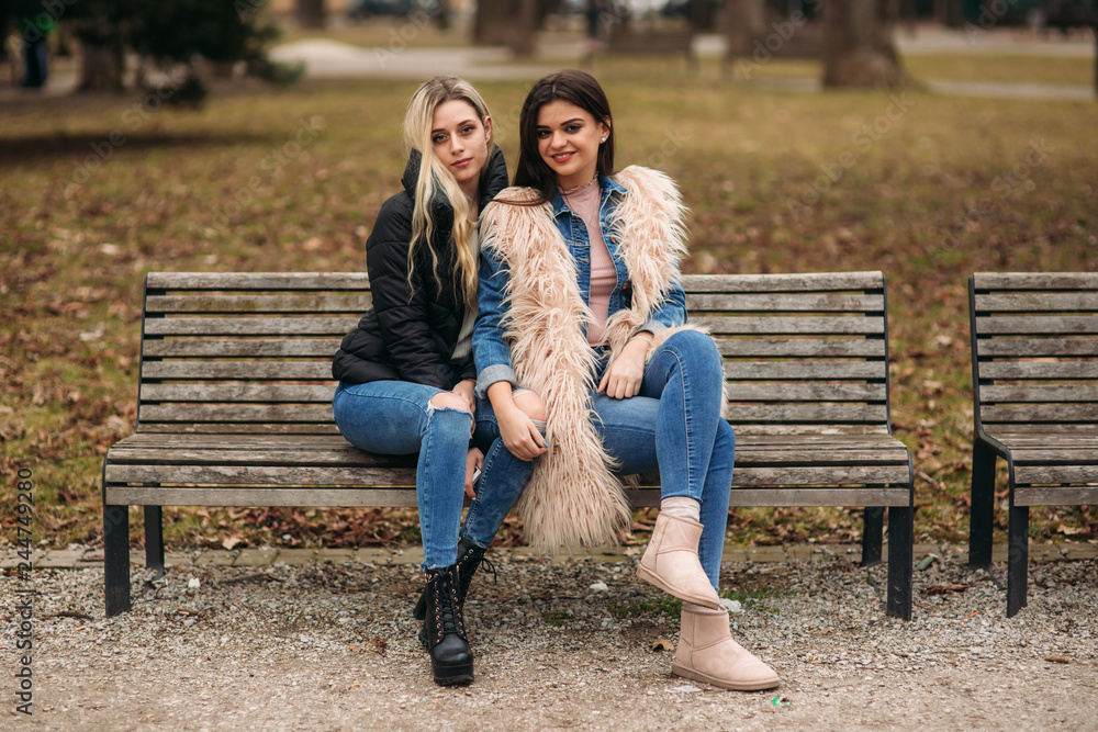 Two girls sitting on the bench outdoors. Autumn weather Two girls sitting on the bench outdoors. Autumn weather
