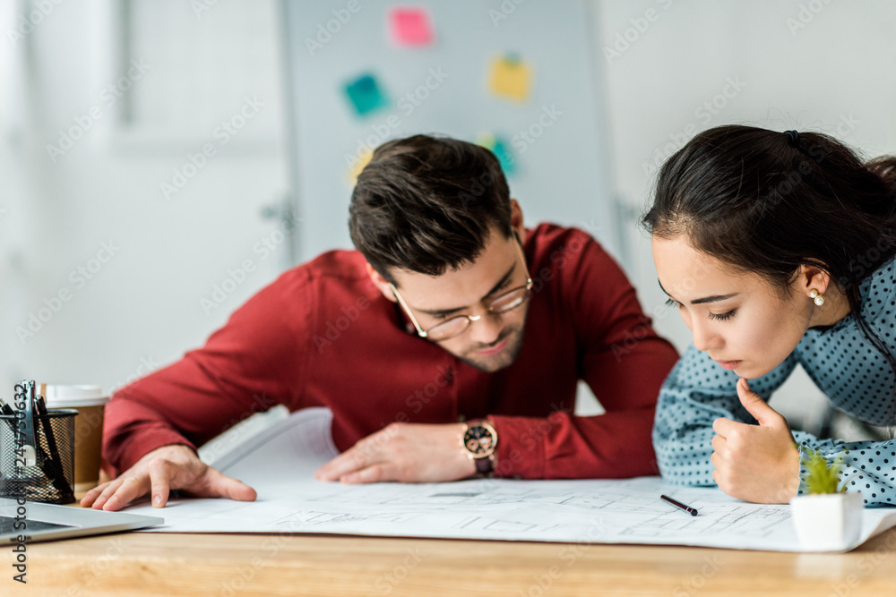focused multicultural couple of architects working on blueprint in office focused multicultural couple of architects working on blueprint in office
