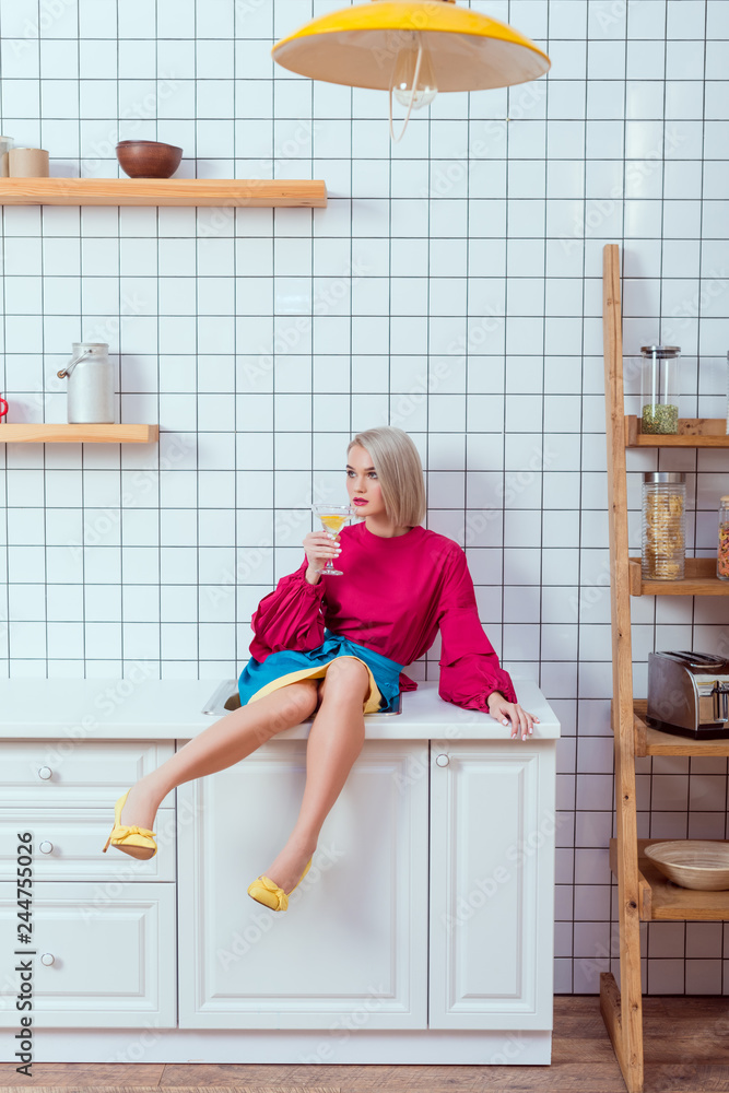 beautiful fashionable woman sitting on kitchen counter with cocktail glass and looking away beautiful fashionable woman sitting on kitchen counter with cocktail glass and looking away