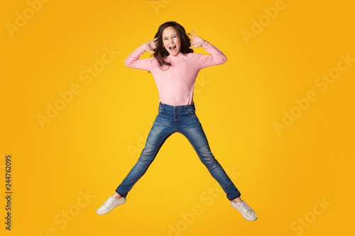 Excited girl jumping and shouting over yellow background