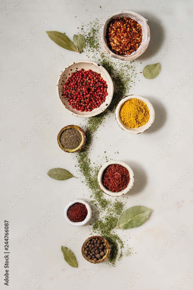 Spices seasoning and herbs variety in ceramic bowls. Different ground peppers, chili pepper, turmeric, bay leaf, cinnamon over white marble background. Flat lay, space. Cooking concept Spices seasoning and herbs variety in ceramic bowls. Different ground peppers, chili pepper, turmeric, bay leaf, cinnamon over white marble background. Flat lay, space. Cooking concept