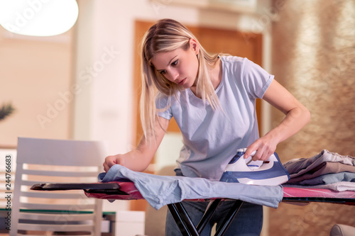 Smiling young woman ironing clothes at home