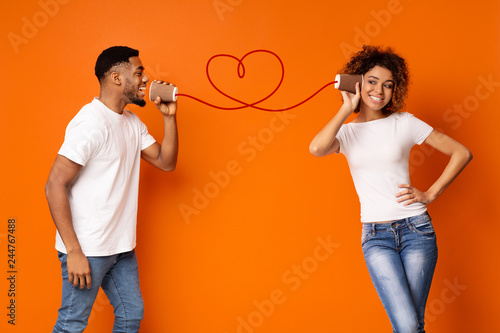 Young black couple with can phone on orange background photo
