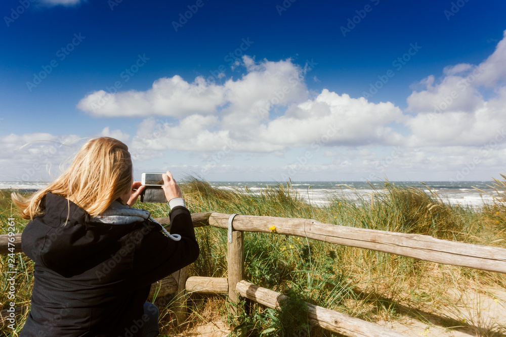 Woman is taking a snapshot of the beach the sea and the dunes