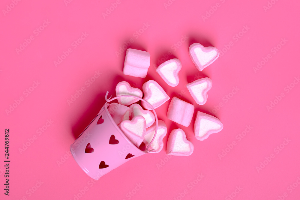 marshmallows  heart shaped candies spilled from a pink iron bucketon a pink background Happy Valentine's Day Flat lay Top view
