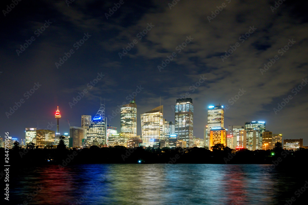 Obraz premium sydney cbd panorama at night, buildings reflection in water, dark cloudy night sky