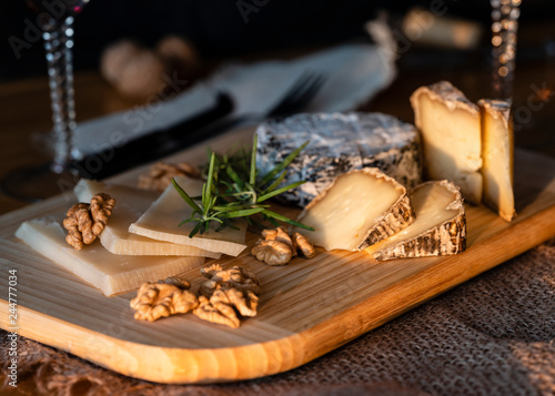 Some kinds of the blue cheeses with halves of the walnuts and rosemary, two glasses with red wines, knife and fork on the wooden desk