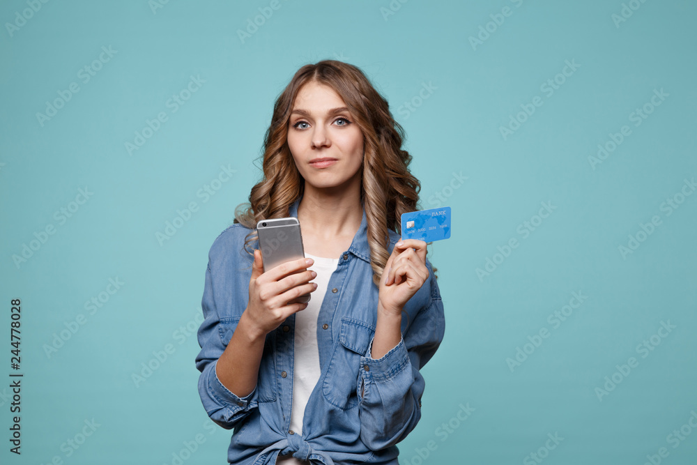 Image of excited young lady isolated over blue background using mobile phone holding credit card. Image of excited young lady isolated over blue background using mobile phone holding credit card.