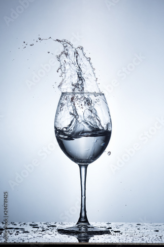 Splashing water on blue background. Wine glass with water.