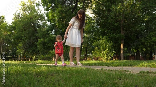 Mom and little daughter are walking along path in summer park. baby's first steps with mom